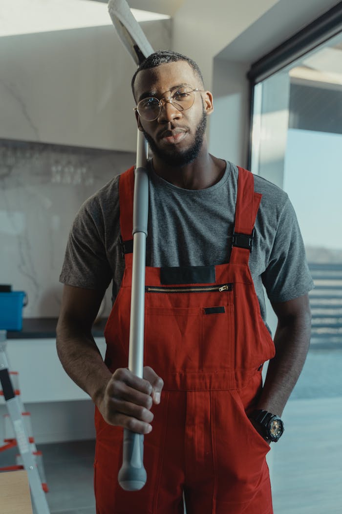 Confident male cleaner posing with cleaning tool in modern interior, showcasing professionalism.
