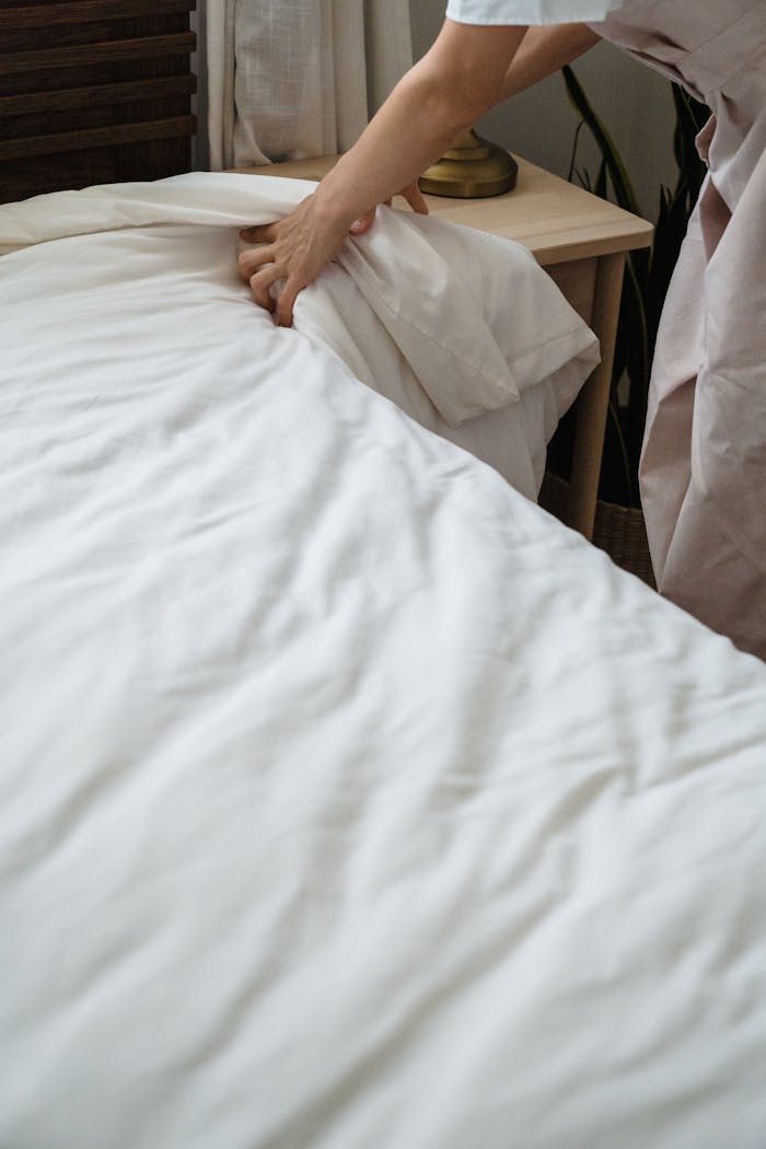 A housekeeper adjusts the bed linens in a tidy bedroom, emphasizing cleanliness and order.